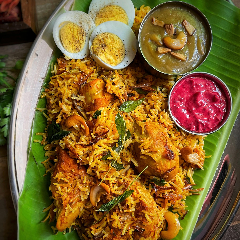 YOYO MOMOSS's chicken biryani with boiled eggs, green curry, and pink raita on a banana leaf.