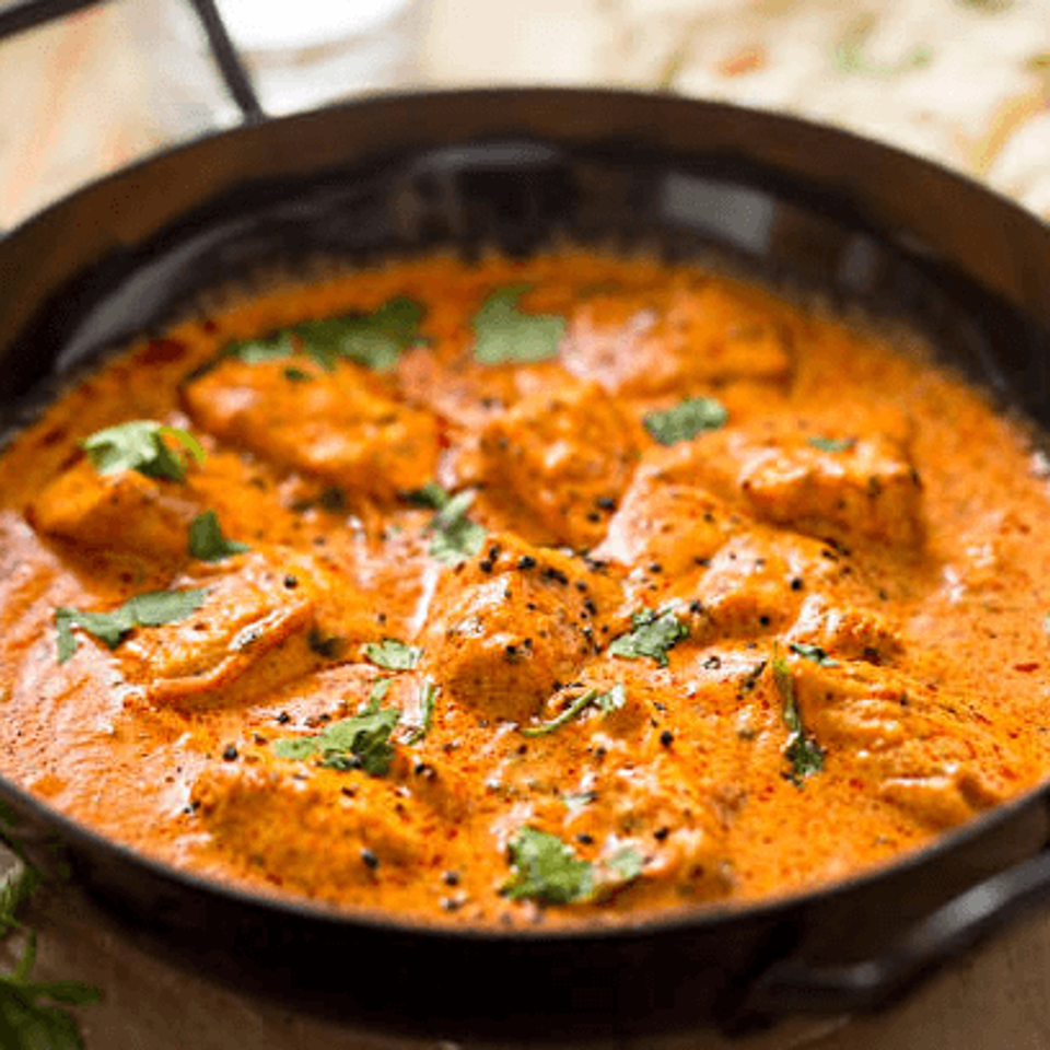 Close-up of YOYO MOMOSS butter chicken, a rich orange curry with chicken pieces and fresh cilantro.